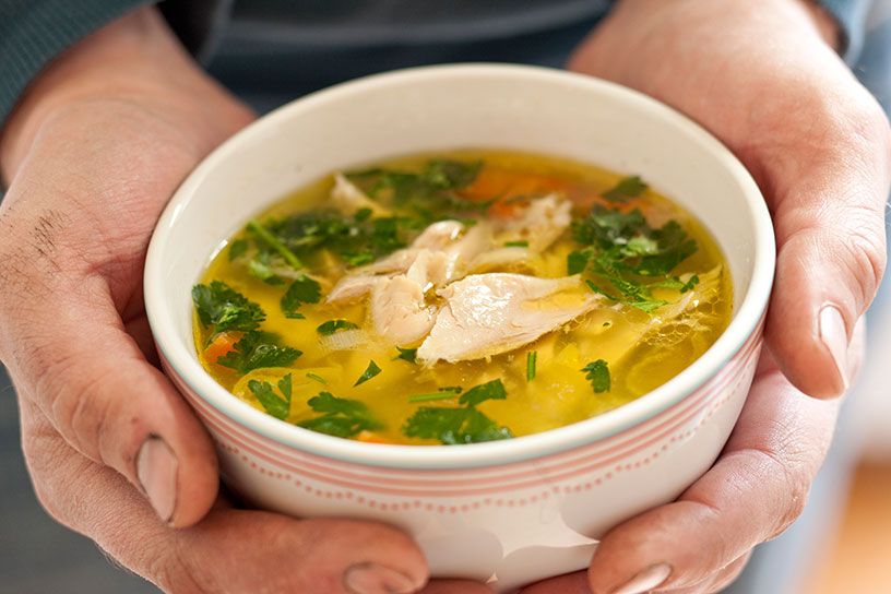 Handen die een kom ouderwetse kippensoep vasthouden